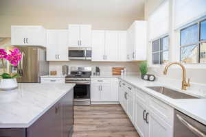 Kitchen with appliances with stainless steel finishes, light stone countertops, sink, and white cabinets