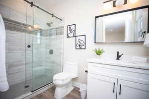 Bathroom featuring an enclosed shower, vanity, wood-type flooring, and toilet