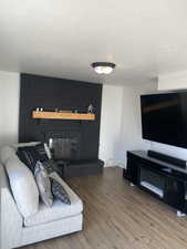 Living room with hardwood / wood-style floors, a textured ceiling, and a brick fireplace