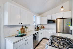 Kitchen with sink, stainless steel appliances, light stone counters, tasteful backsplash, and vaulted ceiling