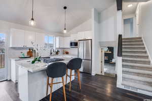 Kitchen featuring sink, white cabinetry, tasteful backsplash, decorative light fixtures, and stainless steel appliances