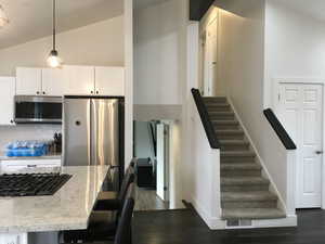 Kitchen with vaulted ceiling, pendant lighting, stainless steel appliances, light stone countertops, and white cabinets