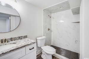 Bathroom with hardwood / wood-style floors, vanity, a tile shower, and toilet