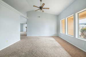 Carpeted spare room featuring vaulted ceiling and ceiling fan