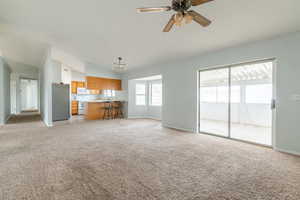 Unfurnished living room with lofted ceiling, ceiling fan with notable chandelier, and light carpet