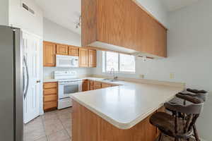 Kitchen featuring vaulted ceiling, sink, light tile patterned floors, kitchen peninsula, and white appliances