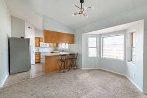 Kitchen featuring sink, white appliances, light carpet, vaulted ceiling, and kitchen peninsula