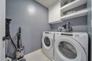 Laundry room featuring cabinets, washing machine and dryer, and light tile patterned floors