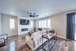 Living room featuring dark wood-type flooring, a large fireplace, and ceiling fan