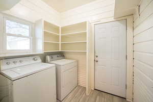 Clothes washing area with independent washer and dryer, light hardwood / wood-style floors, and wood walls