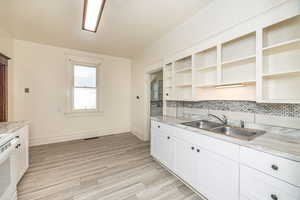 Kitchen with white cabinetry, sink, light stone counters, and white range with electric cooktop