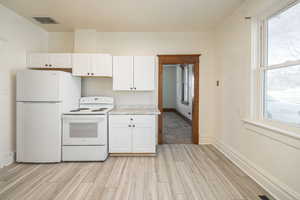 Kitchen with white appliances, light hardwood / wood-style flooring, and white cabinets