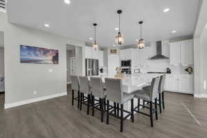 Kitchen featuring appliances with stainless steel finishes, white cabinets, dark hardwood / wood-style flooring, a large island, and wall chimney range hood