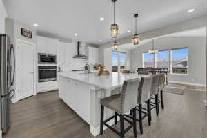 Kitchen with white cabinetry, wall chimney range hood, decorative light fixtures, and stainless steel appliances