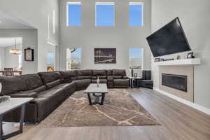 Living room featuring a tiled fireplace, a notable chandelier, wood-type flooring, and a high ceiling