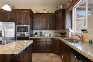 Kitchen with sink, dark brown cabinets, appliances with stainless steel finishes, pendant lighting, and backsplash