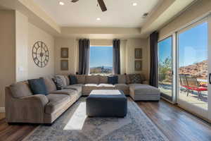 Living room featuring ceiling fan, a tray ceiling, dark wood-type flooring, and a healthy amount of sunlight