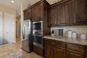 Kitchen with stainless steel refrigerator with ice dispenser, light stone counters, tasteful backsplash, dark brown cabinets, and light tile patterned floors