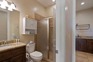 Bathroom featuring a shower with door, vanity, tile patterned floors, and toilet