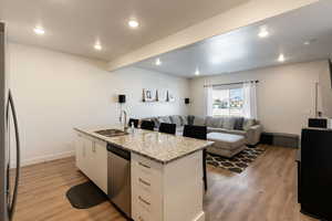 Kitchen featuring sink, white cabinetry, stainless steel appliances, a center island with sink, and light wood-type flooring