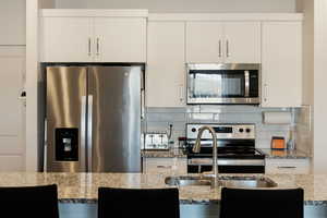 Kitchen with tasteful backsplash, appliances with stainless steel finishes, and white cabinets