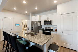 Kitchen featuring sink, hardwood / wood-style floors, stainless steel appliances, white cabinets, and a center island with sink