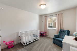 Carpeted bedroom with a crib and a textured ceiling