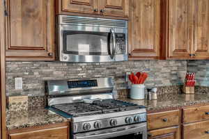 Kitchen with dark stone countertops, stainless steel appliances, and backsplash