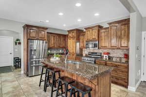 Kitchen with an island with sink, sink, backsplash, dark stone counters, and stainless steel appliances