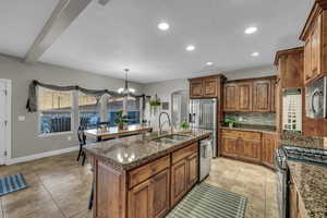 Kitchen featuring sink, appliances with stainless steel finishes, a kitchen island with sink, tasteful backsplash, and a notable chandelier