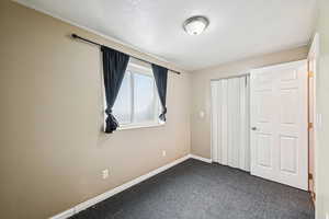 Unfurnished bedroom featuring dark colored carpet, a textured ceiling, and a closet