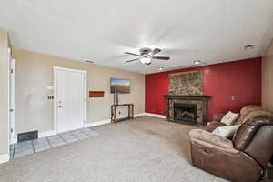 Carpeted living room with ceiling fan and a stone fireplace