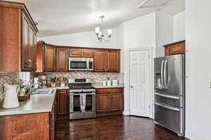 Kitchen featuring decorative light fixtures, lofted ceiling, sink, decorative backsplash, and stainless steel appliances