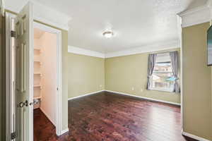 Empty room featuring dark hardwood / wood-style flooring, crown molding, and a textured ceiling