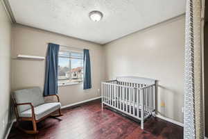 Bedroom with a crib, crown molding, dark wood-type flooring, and a textured ceiling