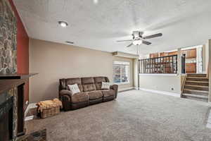 Living room featuring a stone fireplace, a textured ceiling, ceiling fan, and carpet