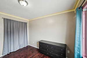 Unfurnished bedroom with crown molding, dark wood-type flooring, and a textured ceiling