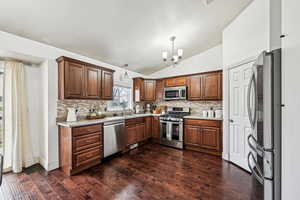 Kitchen featuring pendant lighting, decorative backsplash, vaulted ceiling, and stainless steel appliances