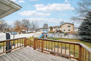 Wooden deck featuring a playground, a shed, and a lawn