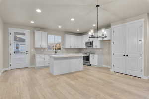 Kitchen with white cabinetry, decorative light fixtures, light wood-type flooring, appliances with stainless steel finishes, and a kitchen island