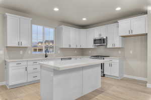 Kitchen with white cabinetry, sink, a center island, stainless steel appliances, and light wood-type flooring