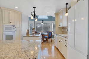 Kitchen with white appliances, light stone counters, a kitchen island, decorative light fixtures, and light wood-type flooring