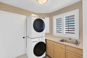 Laundry room with light tile patterned flooring, cabinets, stacked washer and clothes dryer, and sink