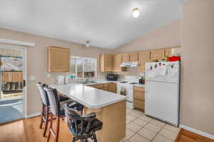 Kitchen featuring a breakfast bar, sink, kitchen peninsula, light brown cabinets, and white appliances