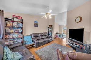 Living room with hardwood / wood-style flooring, vaulted ceiling, and ceiling fan with notable chandelier