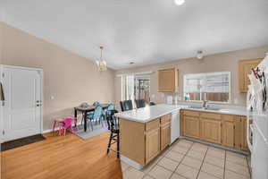 Kitchen featuring sink, white appliances, hanging light fixtures, a kitchen bar, and kitchen peninsula