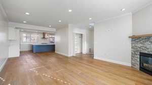 Unfurnished living room featuring ornamental molding, a stone fireplace, and light hardwood / wood-style floors