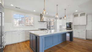 Kitchen with light stone countertops, a kitchen island with sink, exhaust hood, and white cabinets