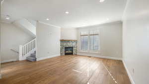 Unfurnished living room featuring crown molding, a stone fireplace, and light hardwood / wood-style floors