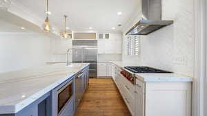 Kitchen with white cabinetry, built in appliances, pendant lighting, decorative backsplash, and exhaust hood